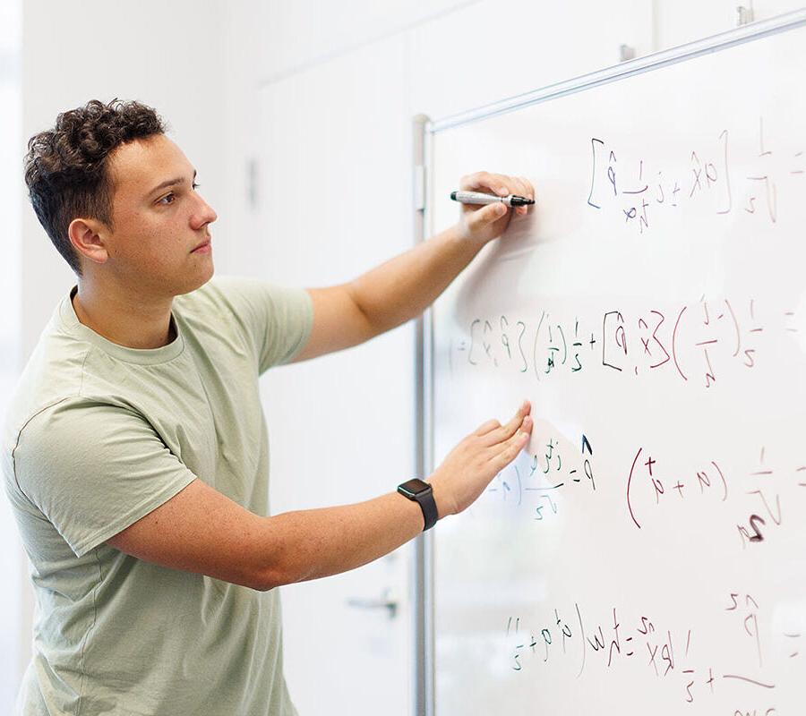 Student from engineering concentration in general engineering program writes equations on a whiteboard.